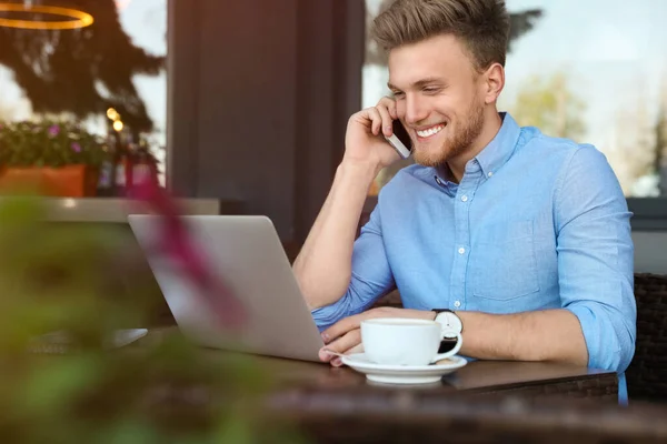 Knappe jongeman met laptop zittend aan tafel in cafe buiten — Stockfoto