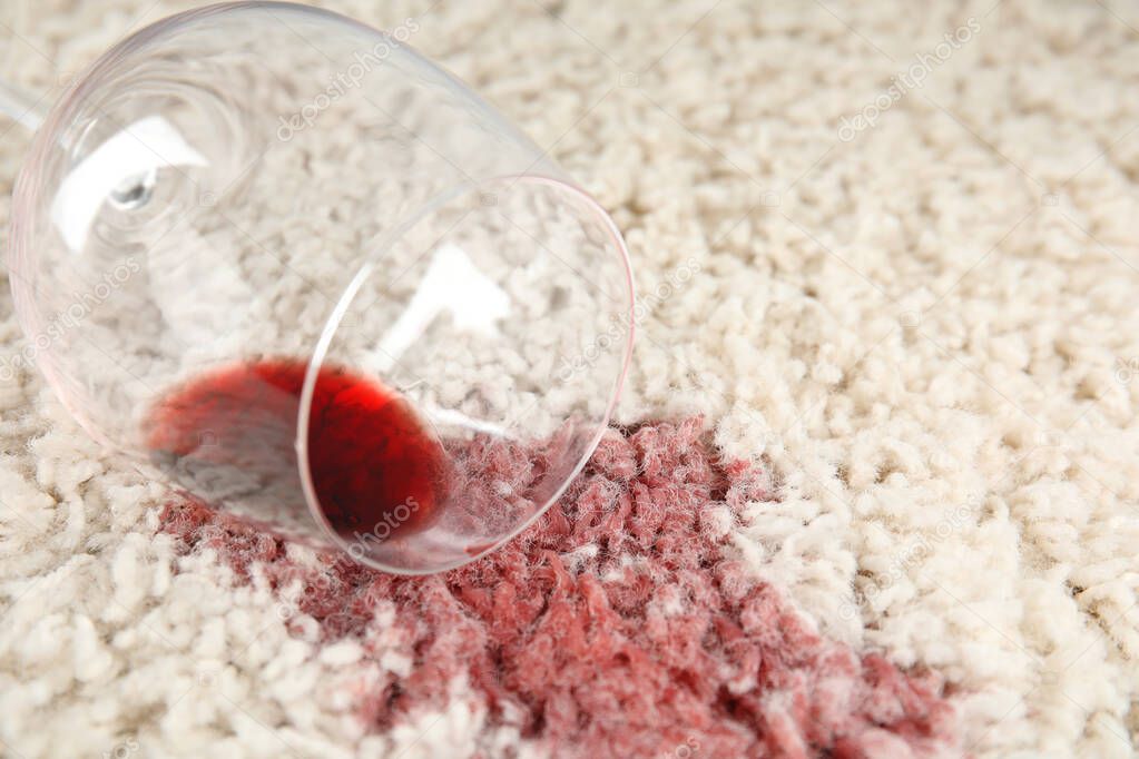 Overturned glass and spilled exquisite red wine on soft carpet, closeup. Space for text
