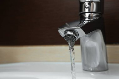 Kapalı alandaki musluktan akan suyun yakın görüntüsü. Metin için boşluk