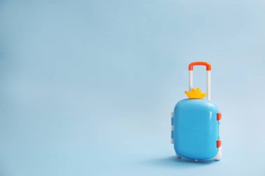 Stylish child suitcase with toy on blue background, space for text