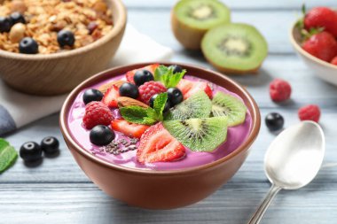 Beyaz ahşap masada servis edilen tatlı kasesinde meyve ve chia tohumlu lezzetli acai smoothie.