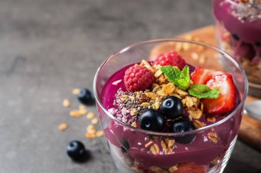 Granola ve böğürtlenli lezzetli acai tatlısı. Gri masada servis ediliyor. Yakın plan. Metin için boşluk