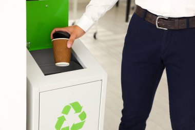 Ofiste kahve bardağını geri dönüşüm kutusuna atan genç adam, yakın çekim.