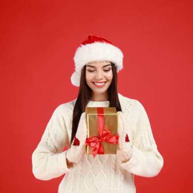 Kırmızı arka planda Noel Baba şapkalı mutlu genç kadın.