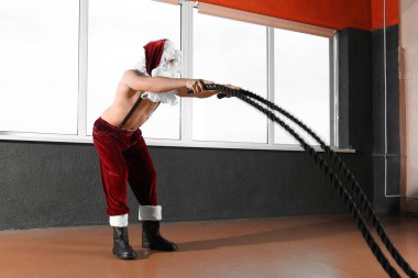 Genç üstsüz Noel Baba modern spor salonunda iplerle antrenman yapıyor.