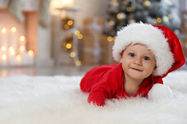 Evde yerde Noel Baba şapkası takan küçük bir bebek. İlk Noel
