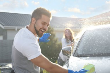 Mutlu çift araba yıkıyor ve güneşli bir günde arka bahçede eğleniyor.