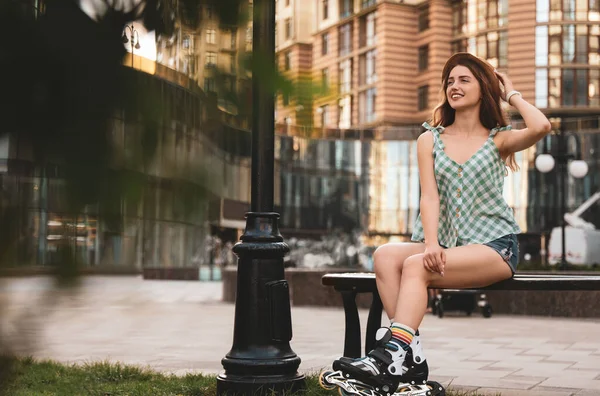 Όμορφη νεαρή γυναίκα με πατίνια που κάθεται στον πάγκο σε εξωτερικούς χώρους, χώρο για κείμενο — Φωτογραφία Αρχείου