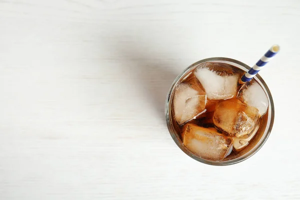 Glass of refreshing soda drink with ice cubes and straw on white wooden background, top view. Space for text — Stock Photo, Image