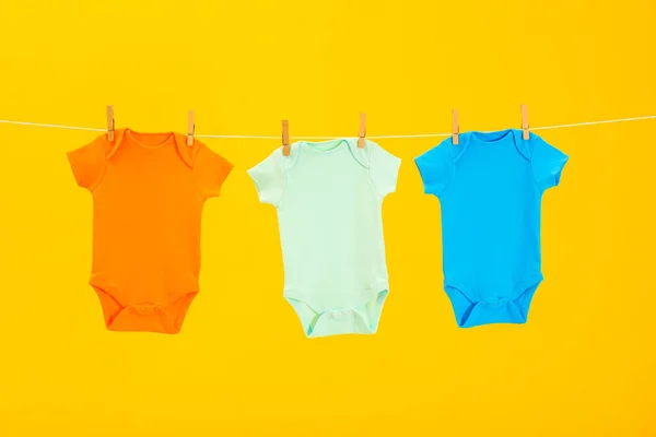 Bebê onesies pendurado na linha de roupas contra fundo amarelo — Fotografia de Stock