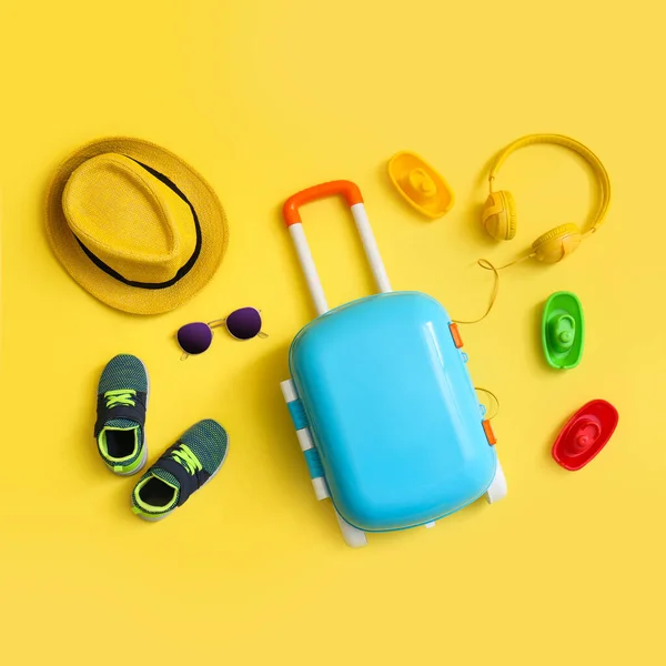 Kompozycja płaska z niebieską walizką i akcesoriami dla dzieci na żółtym tle. Wakacje — Zdjęcie stockowe