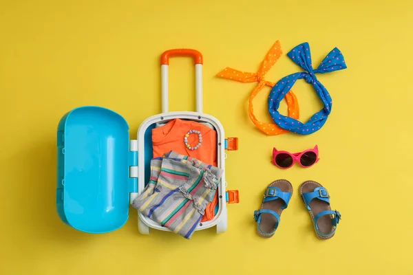 Плоска композиція з синьою валізою та дитячими аксесуарами на жовтому тлі. Літні канікули — стокове фото