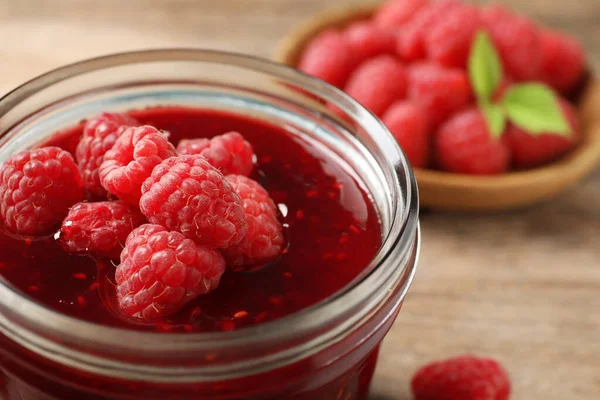 Glass jar of sweet jam with ripe raspberries on wooden table, closeup — Stock Photo, Image