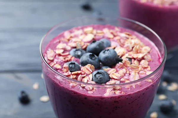 Vidrio con delicioso batido de arándanos con granola en la mesa de madera azul, primer plano —  Fotos de Stock