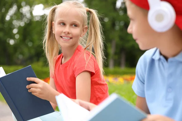 Garoto bonito em fones de ouvido e livros de leitura menina no parque verde — Fotografia de Stock