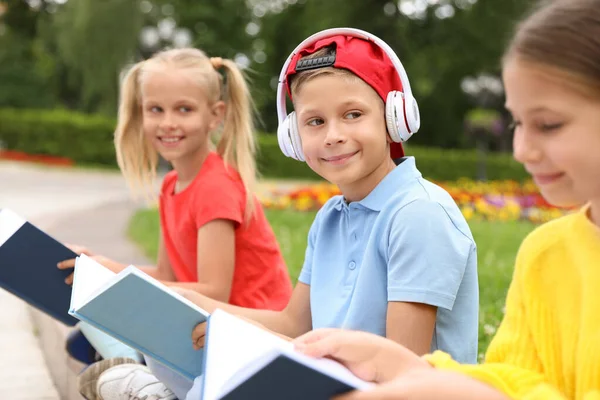 Netter Junge mit Kopfhörern und Mädchen lesen Bücher im grünen Park — Stockfoto