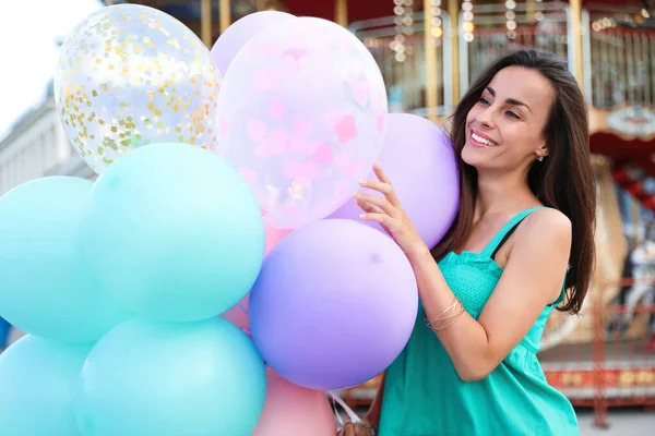 Attraktive junge Frau mit bunten Luftballons in der Nähe von Karussell — Stockfoto