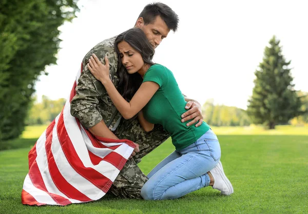 Homem de uniforme militar com bandeira americana abraçando sua esposa no parque verde — Fotografia de Stock