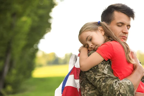 Apa katonai egyenruhában, amerikai zászlóval öleli a lányát a napos parkban. — Stock Fotó