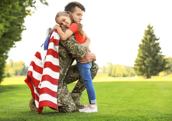 Pai de uniforme militar com bandeira americana abraçando sua filha no parque ensolarado — Fotografia de Stock