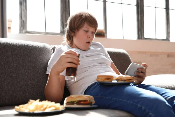 Overweight boy with fast food on sofa at home — Stock Photo, Image