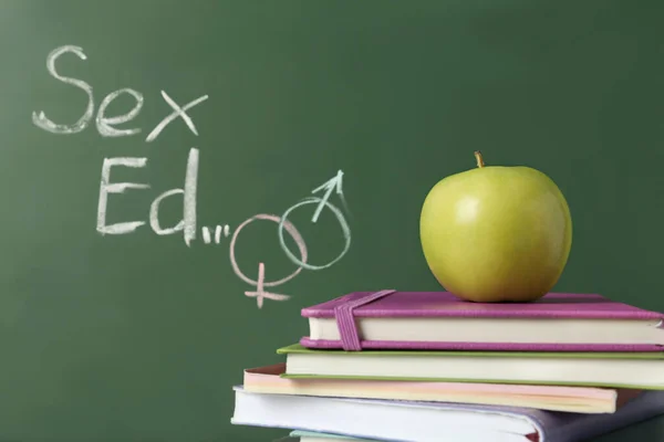 Books and apple near chalkboard with phrase \