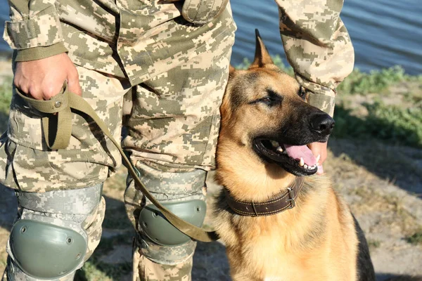 Hombre en uniforme militar con perro pastor alemán cerca del río, vista de cerca — Foto de Stock
