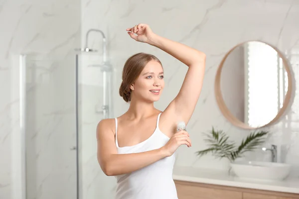 Mujer joven aplicando desodorante roll-on fresco a la axila en el baño — Foto de Stock