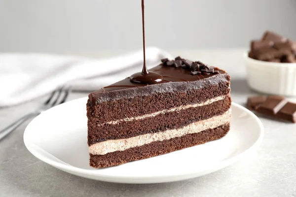 Gießen Schokoladensoße auf leckeren frischen Kuchen auf hellem Tisch, Nahaufnahme — Stockfoto