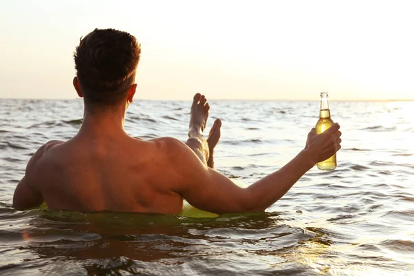 Joven con bebida en anillo inflable en el mar, vista trasera — Foto de Stock