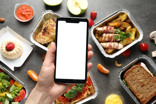 Top view of woman holding smartphone over grey table with lunchboxes, mockup for design. Healthy food delivery — Stock Photo, Image