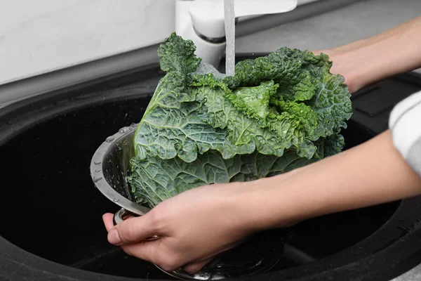 Woman washing fresh green savoy cabbage under tap water in kitchen sink, closeup