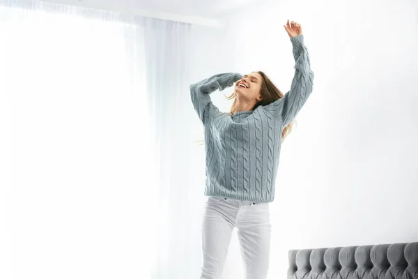 Mujer joven en suéter caliente saltando en la cama en casa — Foto de Stock