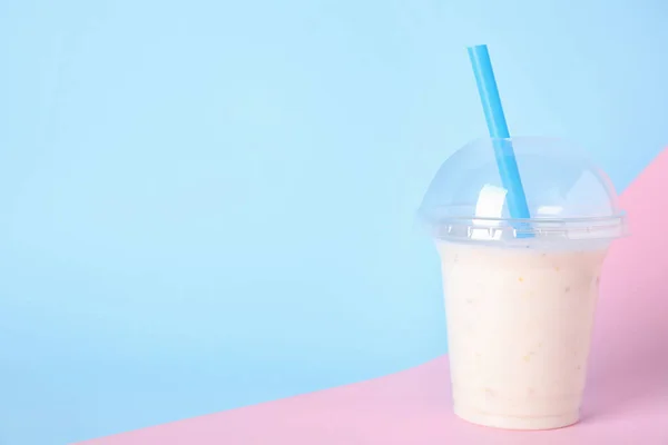 Tasty milk shake in plastic cup on color background. Space for text