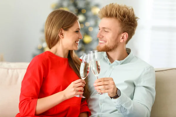 Glückliches junges Paar mit Gläsern Champagner auf dem heimischen Sofa. Weihnachtsfeier — Stockfoto