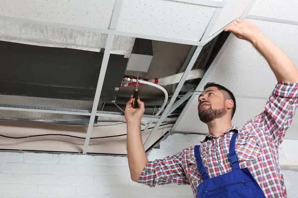 Técnico profissional reparando teto montado ar condicionado dentro de casa — Fotografia de Stock