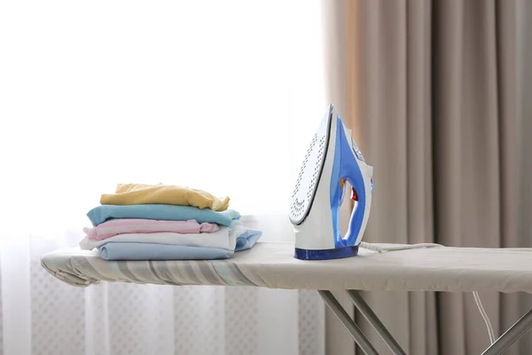Deska z nowoczesnym żelaza i czyste ubrania w pomieszczeniach. Dzień prania — Zdjęcie stockowe