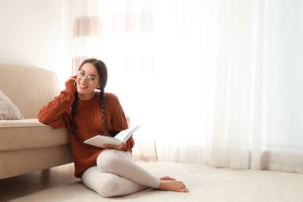 Young woman wearing knitted sweater with book at home — Stok fotoğraf