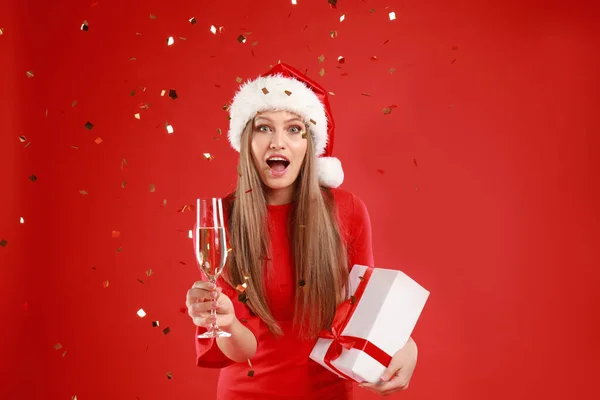 Noel Baba şapkalı ve kırmızı arka planda bir kadeh şampanyası olan duygusal genç kadın. — Stok fotoğraf
