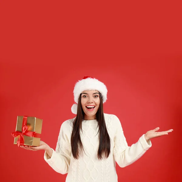 Felice giovane donna a Santa cappello con regalo di Natale su sfondo rosso — Foto Stock