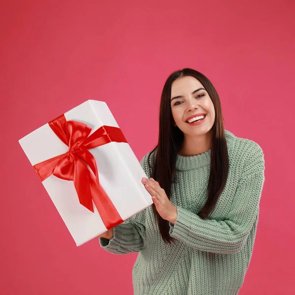 Ευτυχισμένη νεαρή γυναίκα με χριστουγεννιάτικο δώρο σε ροζ φόντο — Φωτογραφία Αρχείου