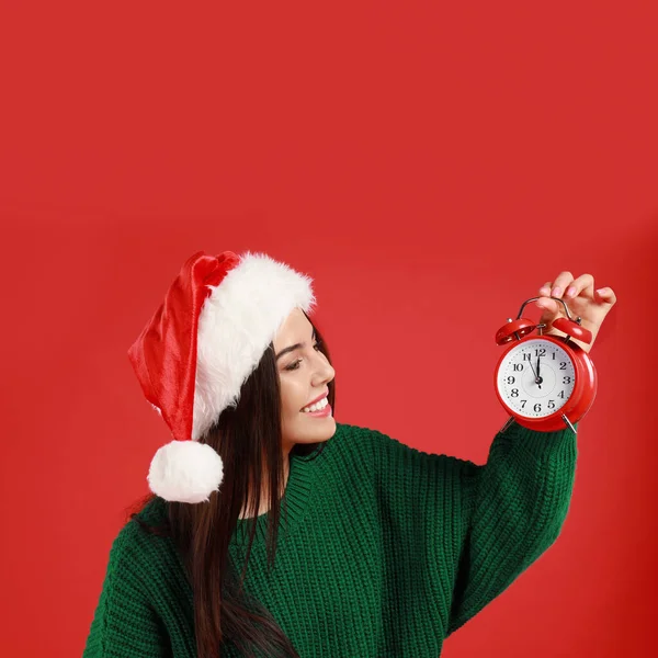 Joyeux jeune femme dans le chapeau de Père Noël avec réveil sur fond rouge. Temps de Noël — Photo