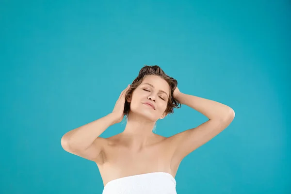 Hermosa joven lavando el cabello sobre fondo azul claro — Foto de Stock