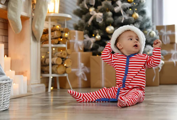 Dziecko w kapeluszu Mikołaja na podłodze w domu. Pierwsze Święta — Zdjęcie stockowe