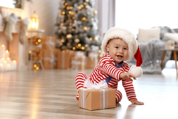 Petit bébé avec chapeau de Père Noël et cadeau de Noël sur le sol à la maison — Photo