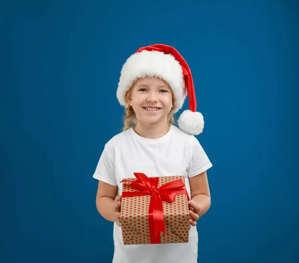 Симпатичный маленький ребенок в шляпе Санты с рождественским подарком на голубом фоне — стоковое фото