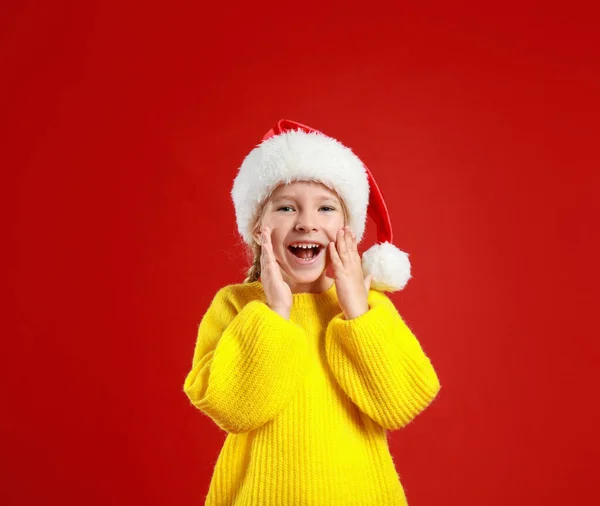 Criança bonita usando chapéu de Papai Noel no fundo vermelho. Natal feriado — Fotografia de Stock