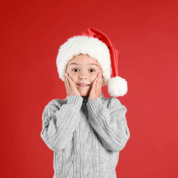 Criança bonita usando chapéu de Papai Noel no fundo vermelho. Natal feriado — Fotografia de Stock