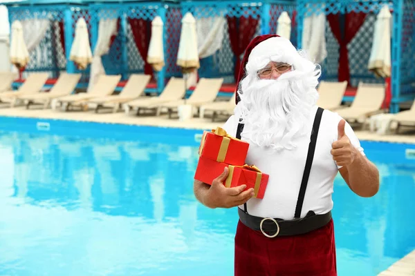 Настоящий Санта-Клаус с подарочными коробками возле бассейна на курорте — стоковое фото