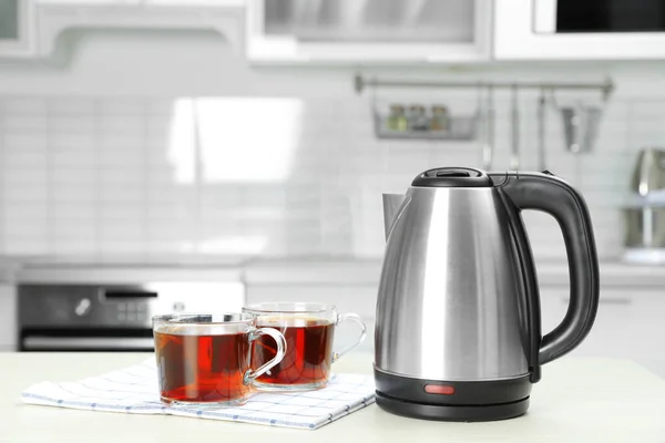 Modern electric kettle and cups of tea on white wooden table in kitchen. Space for text — Stock Photo, Image